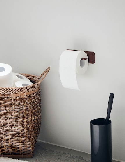 The open toilet paper holder is functional, and its reddish-brown colour brightens up the wall.
