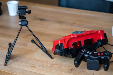 Den Virtual Boy (rechts, mitte) steuerst du mit einem Controller (rechts, unten). Da er sich nicht auf den Kopf spannen lässt, stellst du ihn auf ein Stativ (links).