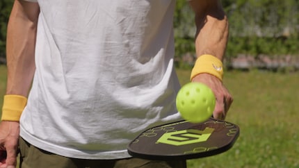 Het pickleball-onderdeel van het spel: een bat van hout, een bal van plastic.